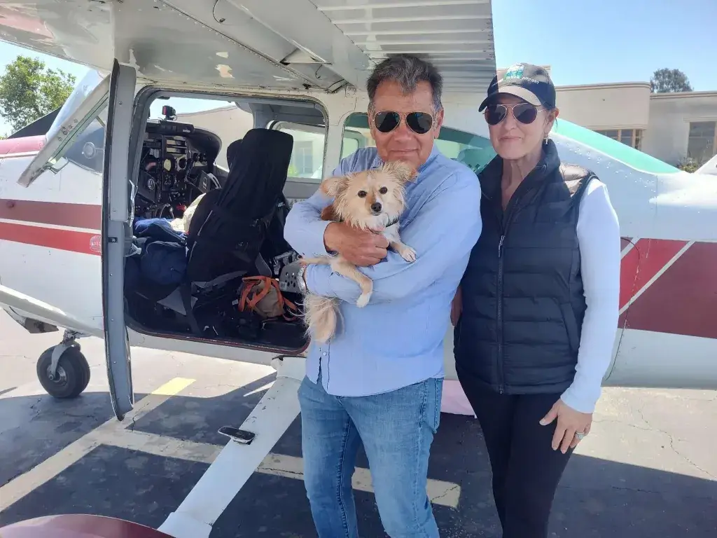 Ken Wayne holding a rescued dog in front of a Flying Tails plane